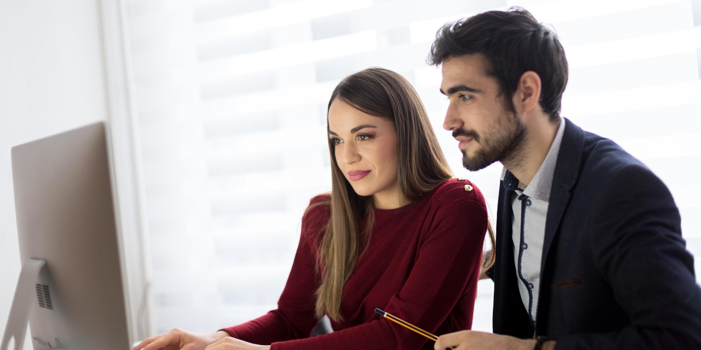two people in business casual clothing smiling at a computer screen