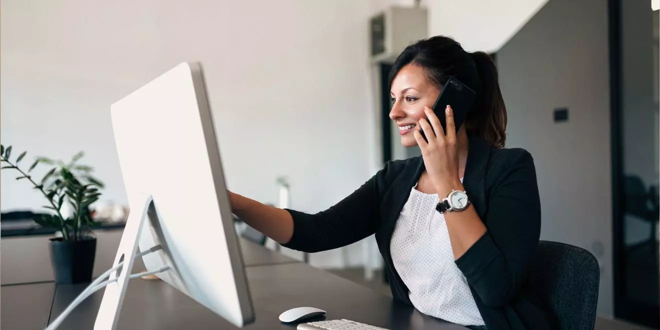 a professional looking at a desktop screen and talking on the phone