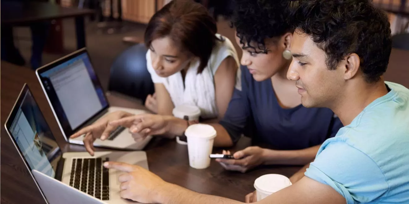 three people gathered around laptops