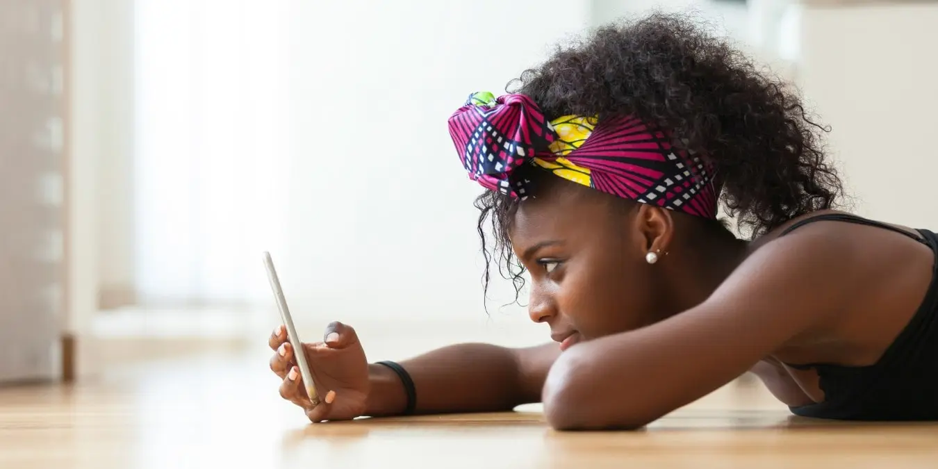 a student resting her head and arms across a desk while smiling at a cell phone