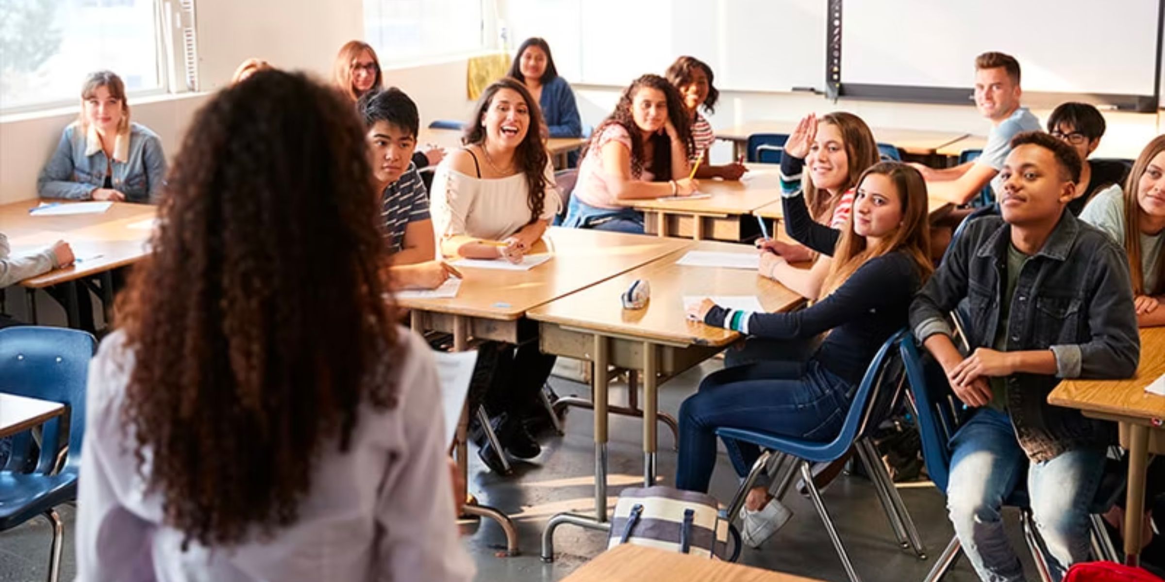 A group of students at their desks with hands up to answer a question