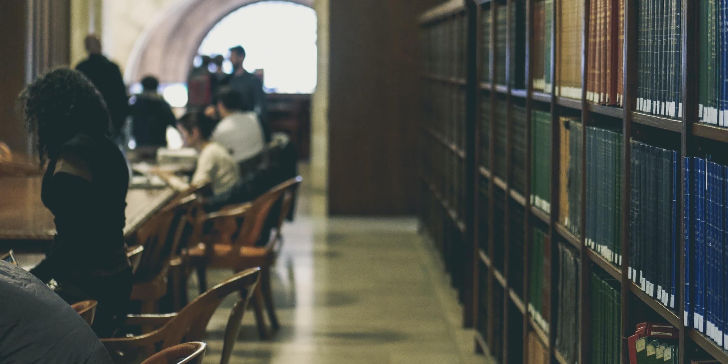 Students studying at library desks with rows of books behind them