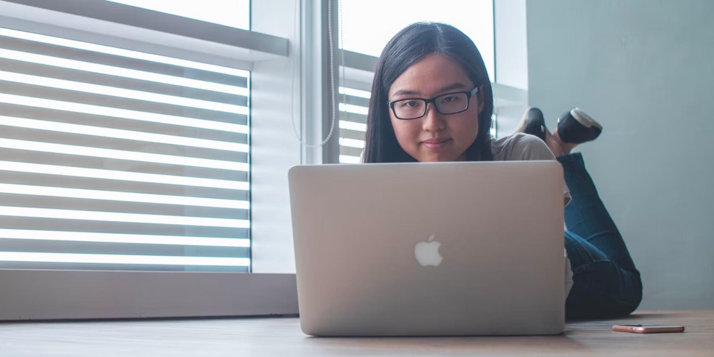 a student lying down on their stomach while typing on a laptop