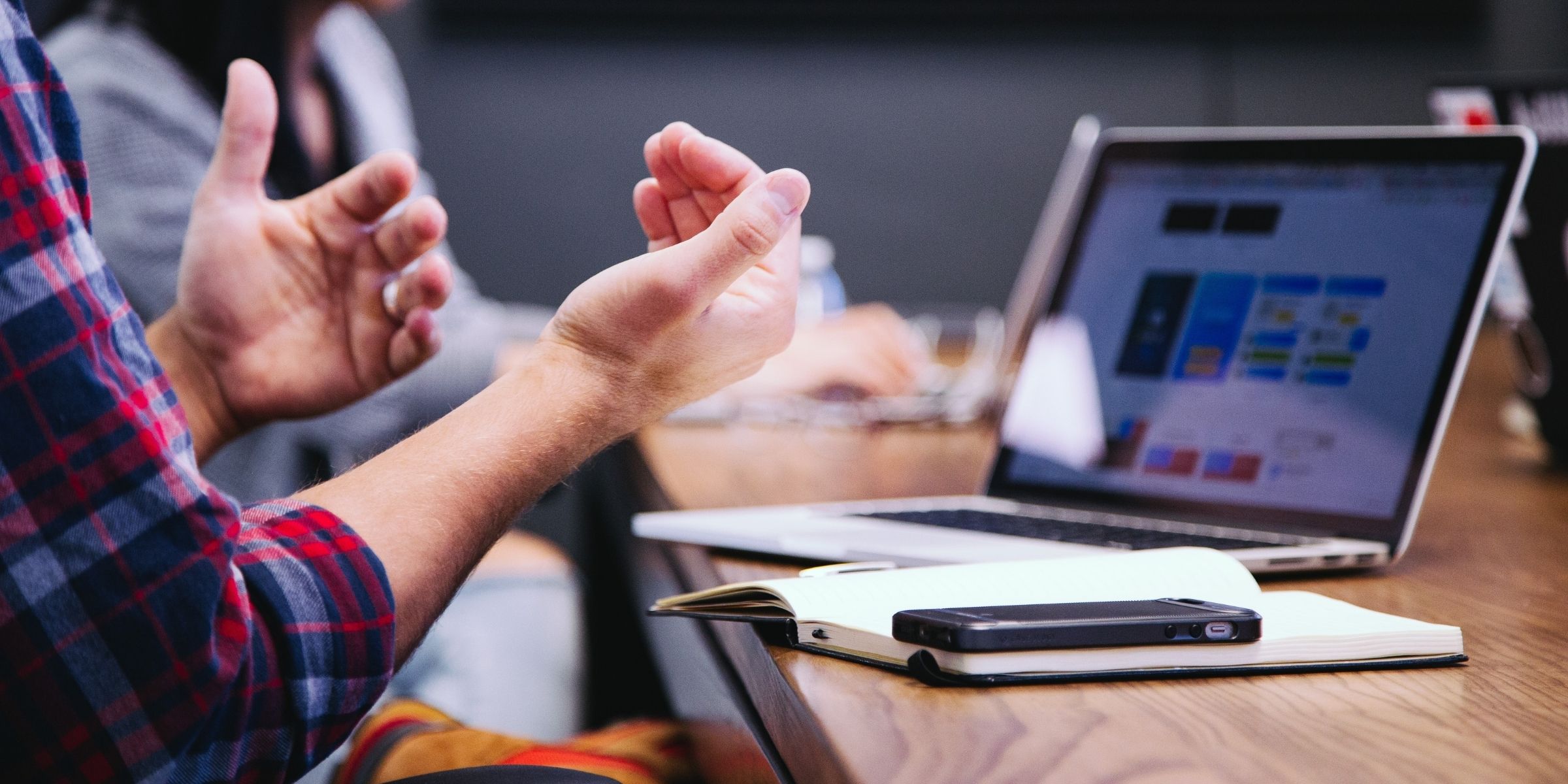 laptop open on a table with a student's hands gesturing in front of it
