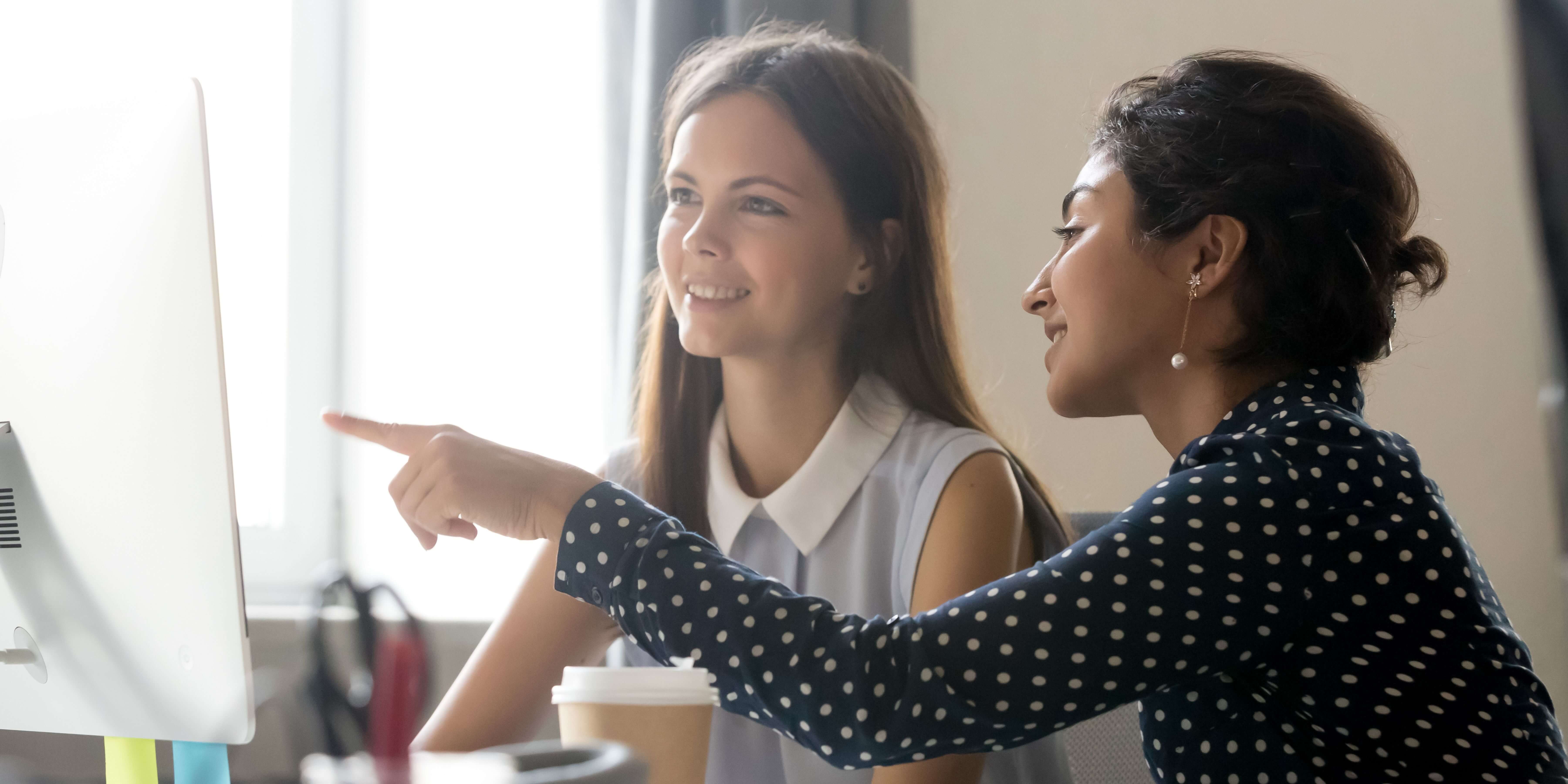 a student smiling at a laptop as an advisor looks over her shoulder